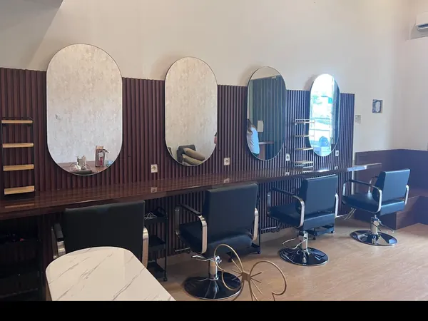 Interior Beausera dari sisi lain: cermin oval berjajar di dinding kayu, kursi salon hitam, dan meja marmer di depan