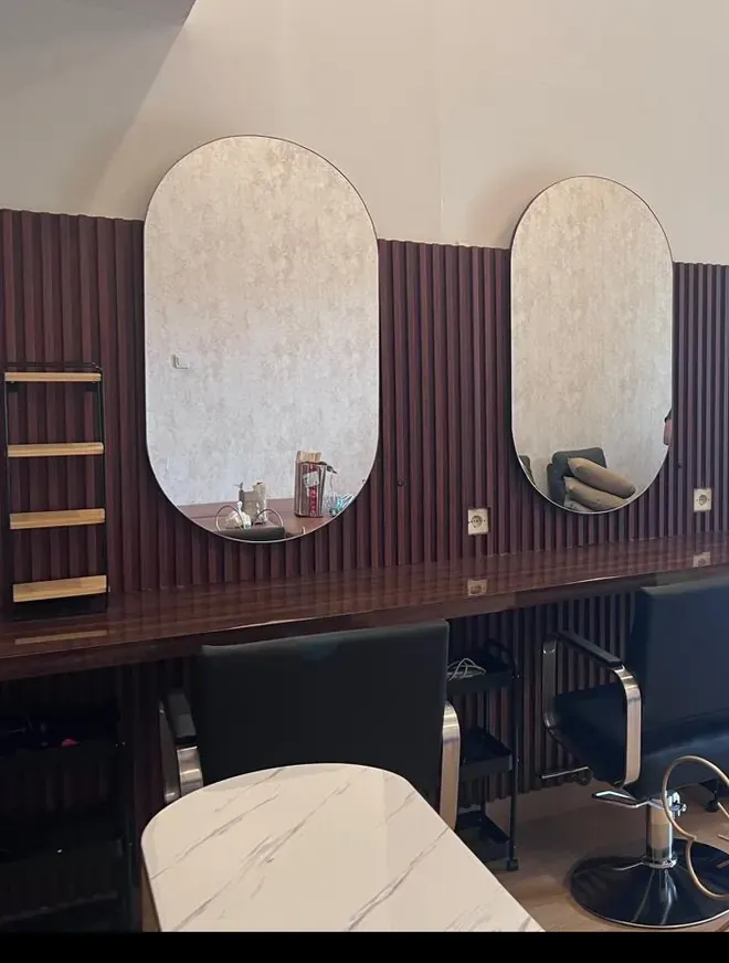 Ruang perawatan rambut Beausera: dua cermin oval di dinding kayu bergaris dan kursi salon hitam