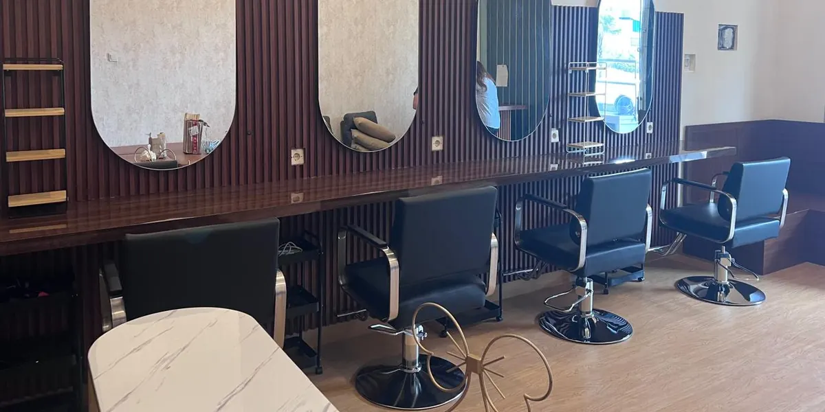 Baris stasiun rambut Beausera: empat cermin oval di dinding kayu bergaris, kursi salon hitam beroda, dan meja kayu panjang