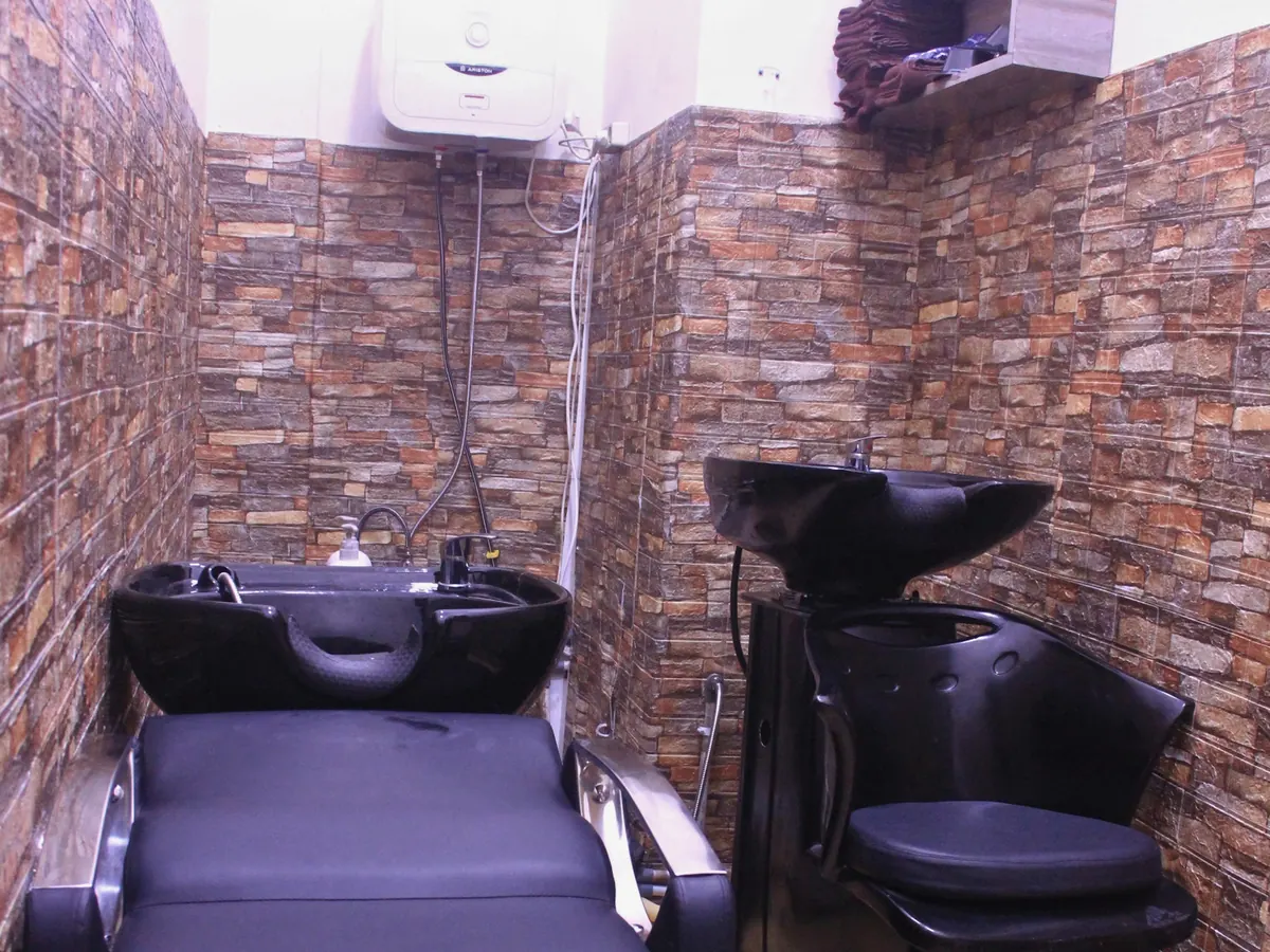 Ruang cuci rambut Beausera dengan dua wastafel hitam, dinding bermotif batu, dan pemanas air di dinding